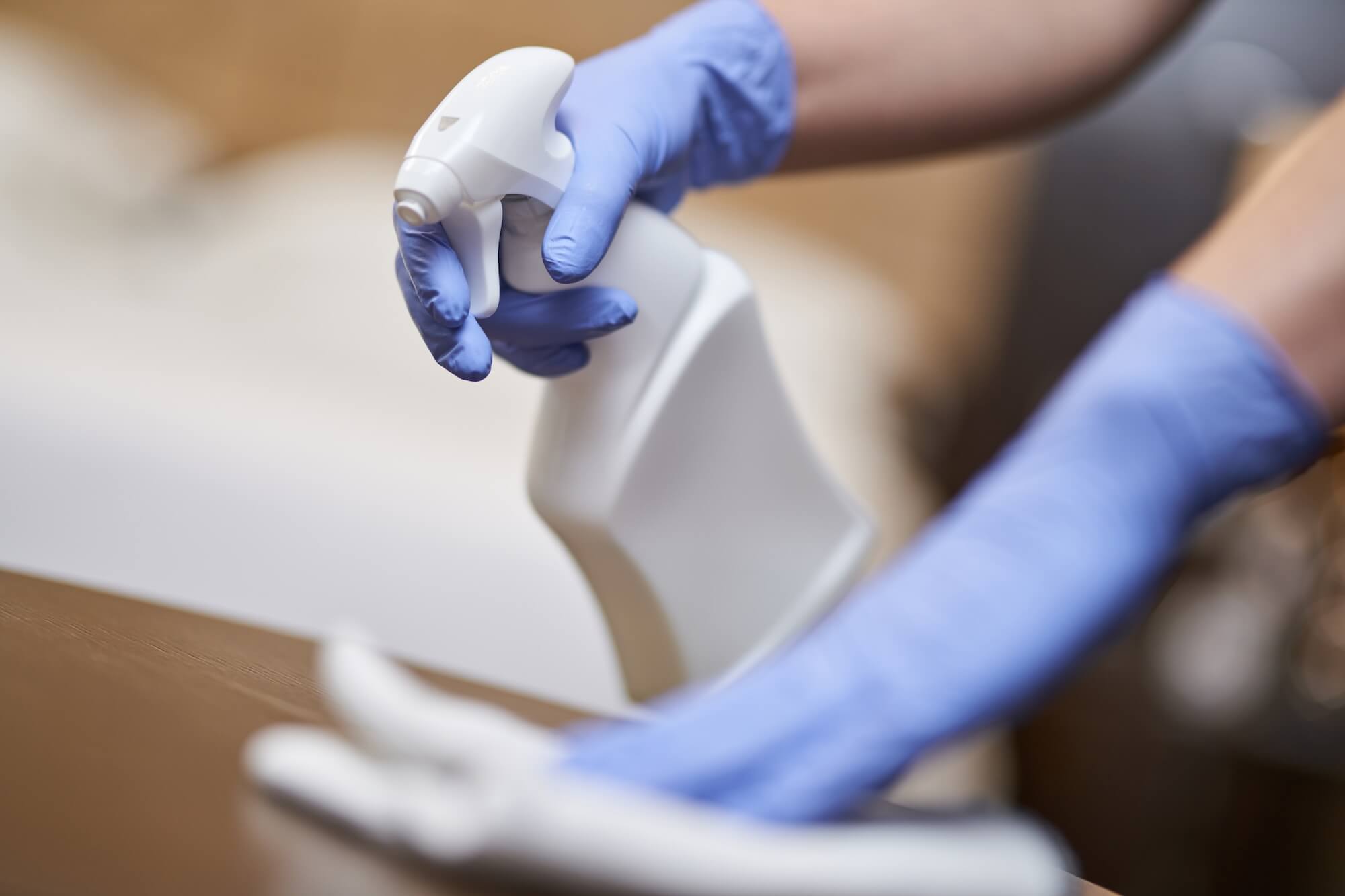 En person med blå skyddshandskar sprayar rengöringsmedel och torkar av en yta för noggrann desinfektion och rengöring.